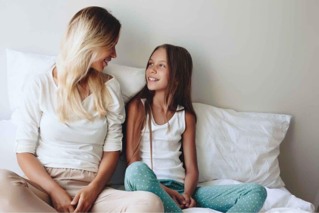 Une maman sourit à sa fille assises sur un lit dans un moment de complicité et d'amour familial